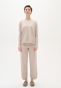 Maglione in maglia beige, ampio e con maniche lunghe, con scollo rotondo, abbinato a pantaloni larghi coordinati e scarpe slip-on.