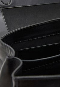 Interior de bolso de cuero negro que muestra una textura suave, múltiples compartimentos y detalles de costura, con un diseño minimalista.