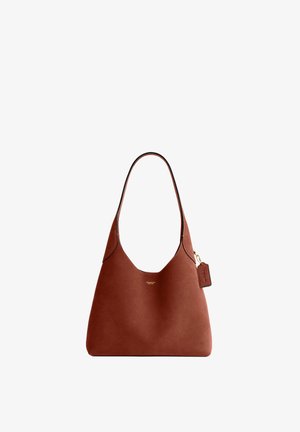 Sac à main Coach en cuir marron avec une bandoulière unique et une petite étiquette de marque suspendue sur le côté droit.