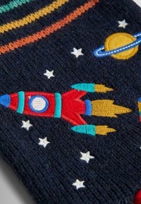 Strikket stof med en mørk marineblå baggrund, broderet med raketter, planeter, stjerner og farverige striber. Raketten er rød med blå og gule detaljer.