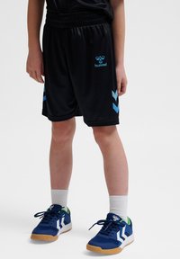 Zwarte shorts met blauwe accenten, gemaakt van lichtgewicht materiaal, met een elastische tailleband en logo. Gedragen met blauw-witte sneakers.