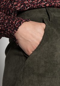 Pantalons en velours côtelé vert olive avec une poche latérale, associés à un haut à manches longues à motif floral texturé avec des poignets froncés.