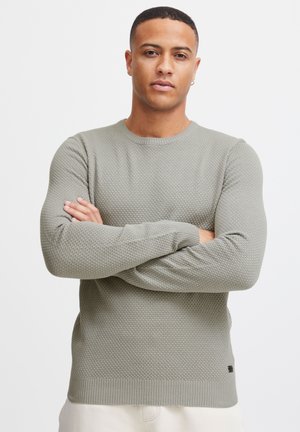 Pulover gri cu textură, cu guler rotund, prezentând un model de fagure și mansete și margine ribbate.
