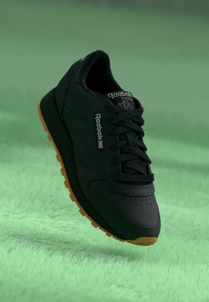 Čierne tenisky s textúrovaným zvrškom, viazaním na šnúrky a gumovou podrážkou. Obsahujú branding Reebok na boku a jazyku.