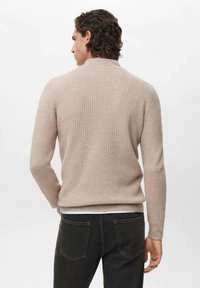 Maglione beige a coste, maniche lunghe, design aderente, tessuto lavorato a maglia testurizzato. Indossato sopra jeans scuri, presenta un semplice scollo tondo.