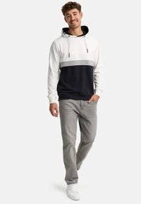 Hættetrøje i hvid, grå og marineblå med snore; parret med lysegrå jeans og hvide sneakers; afslappet pasform, blødt materiale.