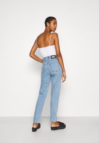 Jeans de cintura alta azul-claro com pernas retas e bolsos traseiros, combinados com uma t-shirt justa branca e sandálias de plataforma pretas.