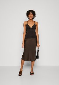 Černý halter top s hlubokým výstřihem do V, spárovaný s hnědou saténovou midi sukni. Průsvitný materiál a hladká textura s přiléhavým siluetou.