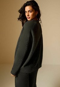 Maglione verde scuro, con texture, dalla vestibilità ampia e spalle scese. Presenta polsini e orlo a costine, abbinato a pantaloni coordinate.
