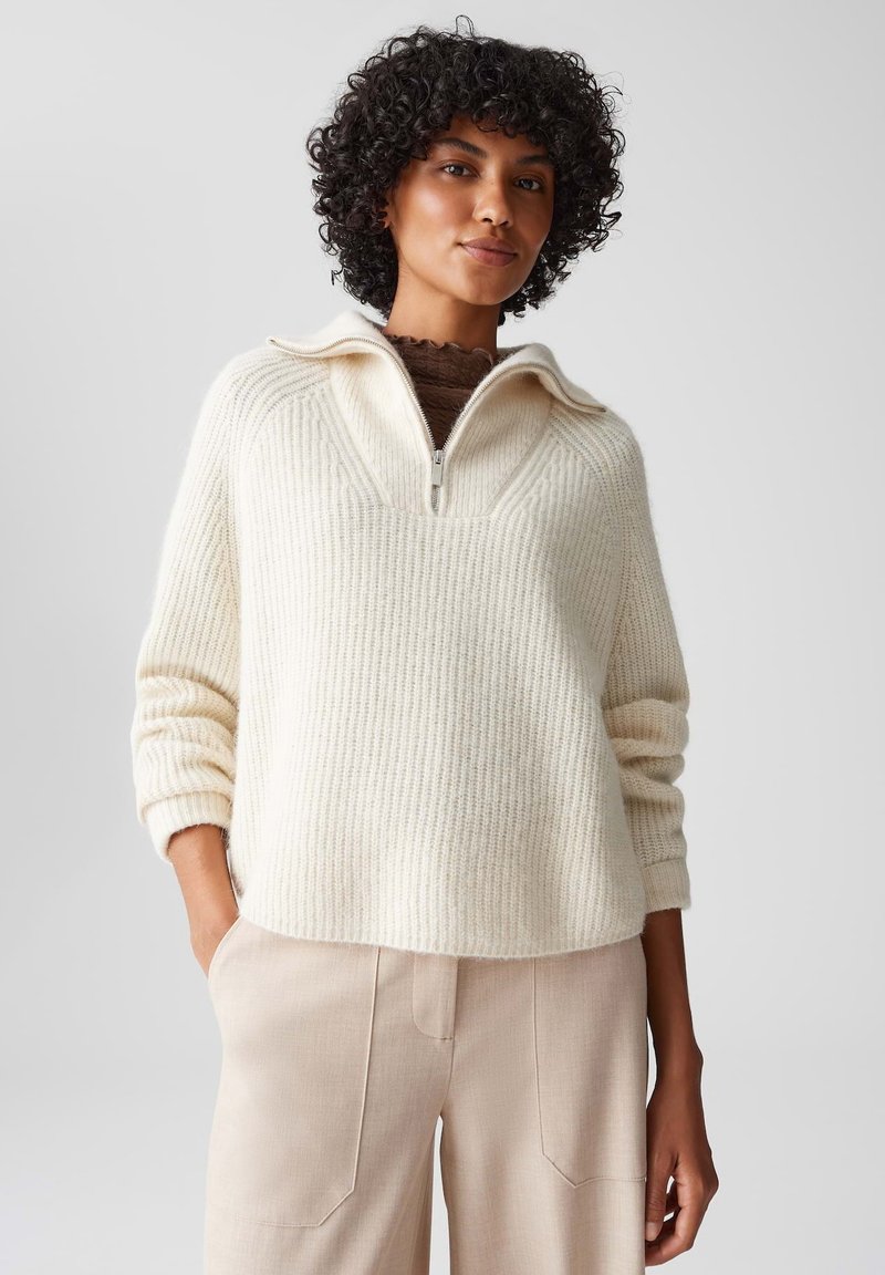 Maglione beige chiaro realizzato in materiale a costine, con colletto a mezza zip, spalle scese e vestibilità rilassata. Abbinato a pantaloni beige.