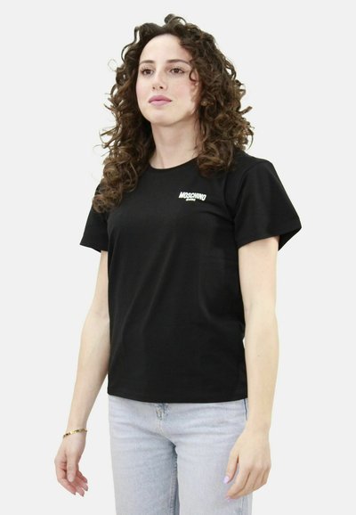 T-shirt in cotone nero con maniche corte e collo rotondo. Logo "Moschino" bianco sul lato sinistro del petto. Indossato con jeans azzurri chiari.