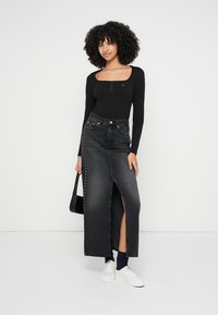 Zwarte henley-top met lange mouwen gecombineerd met een hoogwater zwarte denim rok met een split tot aan de dij en zilveren studs langs de zijkant.