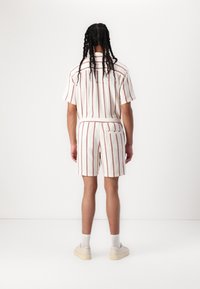 Camisa de manga corta con cuello y pantalones cortos a juego en una tela blanca texturizada con rayas verticales rojas, que presenta un bolsillo trasero.