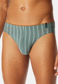 Herren-Schwimmbriefe aus einem hellblauen Stoff mit vertikalen schwarzen Streifen. Ausgestattet mit einem braunen elastischen Bund und einem minimalen Schnitt.