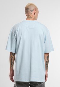 Helede sinine ülepikka T-särk, valminud puuvillast, millel on lühikesed varrukad ja ümar kaelus. Tagantvaates on näha minimalistlik disain ja sile tekstuur.