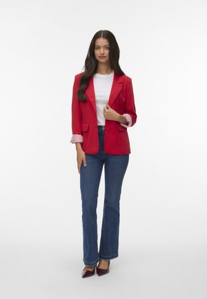 Röd kavaj med en enda knapp, vit topp och blå utsvängda jeans. Har randiga manschettdetaljer och burgundy spetsiga klackskor.