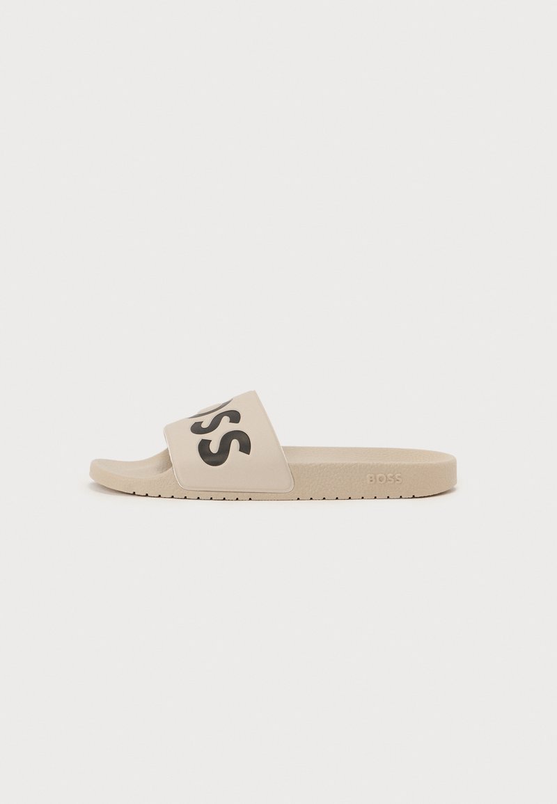 Beige Riemensandale mit schwarzem "BOSS"-Logo auf dem Riemen, glatte Textur, flache Sohle und dezentes Profil für besseren Halt.