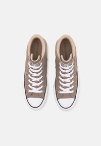 Hnědé plátěné tenisky s bílými tkaničkami a ochranným víčkem, prezentované z pohledu shora, s logem Converse na jazyku.