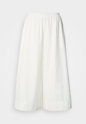 Bijele široke hlače skraćene duljine s elastičnim pojasom i ležernim krojem, prikazane na jednostavnoj pozadini.