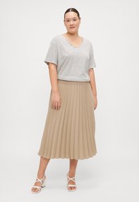 Stripet t-skjorte med kort erme kombinert med en plisserte, knelange beige skjørt. Antrekket er komplimentert av hvite sandaler med remmer.