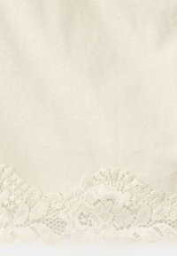 Tissu crème avec une bordure en dentelle florale à bord festonné le long du bord inférieur.