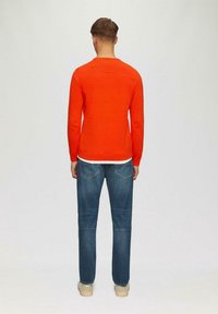 Roter Strickpullover mit langen Ärmeln und Rundhalsausschnitt. Getragen mit blauen Jeans und beigen Schuhen. Schlichtes Design, glatte Textur.
