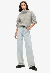 Gray knitted sweater with a turtleneck, paired with light blue wide-leg jeans, accentuated by a black belt and black shoes.
