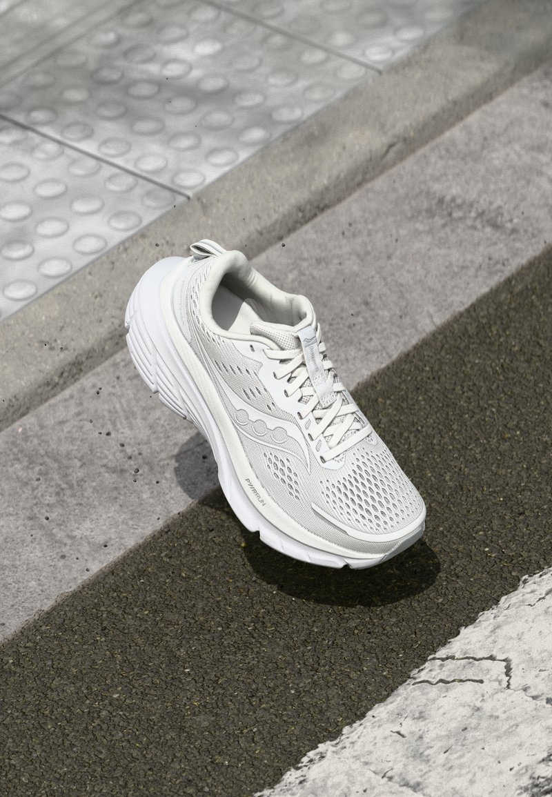 Chaussure de sport blanche avec une tige en mesh pour la respirabilité, semelle rembourrée, accents texturés sur les côtés et un design de laçage sécurisé.