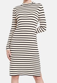 Robe tricotée rayée en crème et noir, avec un col montant montant, des manches longues et des fentes latérales pour plus de liberté de mouvement.