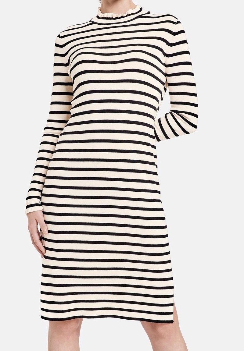 Robe tricotée rayée en crème et noir, avec un col montant montant, des manches longues et des fentes latérales pour plus de liberté de mouvement.