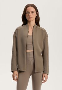Rjava zip-up jakna s stoječim ovratnikom, mehko teksturo in spuščeni rameni, oblečena čez usklajen kratki top in hlače z visokim pasom.