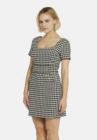 Schwarzes und weißes Hahnentrittmuster-Kleid mit quadratischem Ausschnitt, kurzen Ärmeln und gerafftem Taillenbereich. Verfügt über zwei Fronttaschen mit Knöpfen.