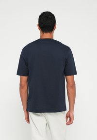 Granatowy bawełniany t-shirt o luźnym kroju, z krótkimi rękawami i okrągłym dekoltem. Gładka faktura, minimalistyczny design, brak widocznych wzorów.