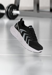 Schwarzer Sportschuh mit strukturiertem Obermaterial, weißer Sohle und reflektierenden Akzenten. Verfügt über ein Schnürdesign und ein auffälliges Logo an der Seite.