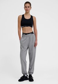 Zwarte sportbeha en grijze joggingbroek met elastische tailleband, met een logo detail. Zwarte sneakers maken de outfit compleet.