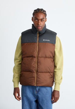 Brown and black padded vest with a high collar, zip closure, and Columbia logo. Worn over a green long-sleeve shirt with blue jeans.