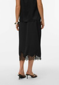 Czarna satynowa spódnica z koronkową lamówką na dole, tworzącą falisty brzeg. Noszona z czarnymi sandałami na obcasie, podkreślająca smukły fason.