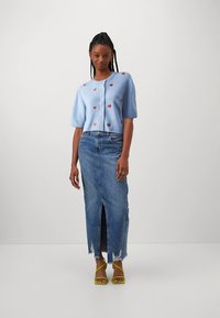 Svetlomodrý pletený sveter s krátkymi rukávmi a motívmi jahôd, v kombinácii s rifľovou sukňou s vysokým rozparkom a žltými sandálmi s remienkami.