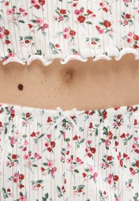 Mi-section avec peau claire, un grain de beauté visible, portant des vêtements en tissu côtelé blanc avec de petits motifs floraux rouges et roses et un petit nœud blanc sur le bas.