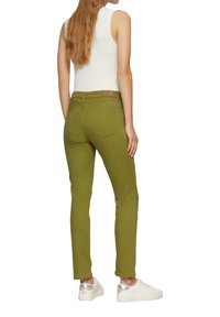Maslinasto zelene slim-fit traperice sa standardnim pojasom, dva stražnja džepa i suptilnim detaljima šivanja, uparenih s bijelim tenisicama.