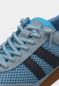 Κοντινό πλάνο γαλάζιου αθλητικού παπουτσιού με ανοιχτό γαλάζιο κορδόνια, σουέτ οπές και σκούρες μπλε λωρίδες στα πλάγια.