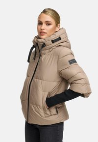Beige pufferjack met een ritssluiting aan de voorkant, een trekkoord-capuchon en zijzakken. Heeft zwarte accenten en een gequilt textuur.