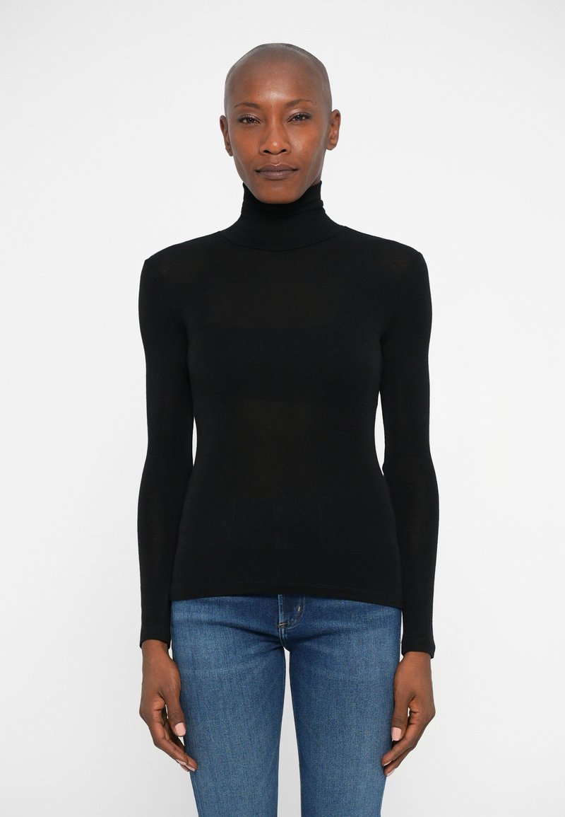Maglione nero a collo alto con maniche lunghe, design aderente e texture liscia, abbinato a jeans blu. Nessun motivo o hardware visibile.