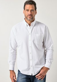 Weißes Hemd mit Knöpfen aus strukturiertem Stoff, langen Ärmeln, einer Tasche auf der linken Brustseite und kontrastierenden Knöpfen, kombiniert mit blauen Jeans.