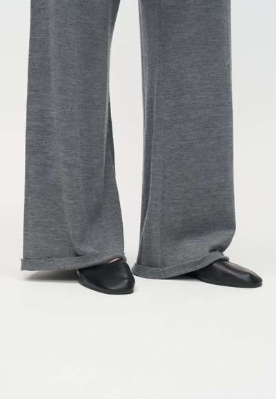 Sivé pletené nohavice s širokými nohavicami zakrývajúce čierne ploché topánky so špicatou špičkou na bielom pozadí.