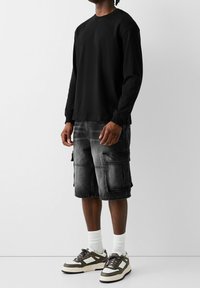 Camisa negra de manga larga combinada con pantalones cortos de carga grises que presentan múltiples bolsillos, junto con zapatillas en tonos de gris y blanco.