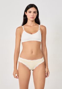 Bralette en coton blanc avec des bretelles réglables, associé à des culottes à carreaux jaunes bordées de dentelle avec un détail en nœud à l'avant.