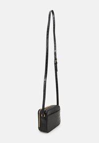 Sac à bandoulière en cuir noir avec un motif crocodile, de forme slim, zipper doré et bandoulière ajustable. Surface texturée et design compact.