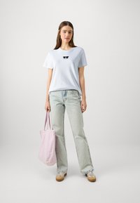 Šviesiai mėlynas medvilninis marškinėlis su juodu akinių nuo saulės piešiniu, derinamas su šviesiai plonais džinsais ir rožine maišelio rankine, turinčia tvirtas rankenas.