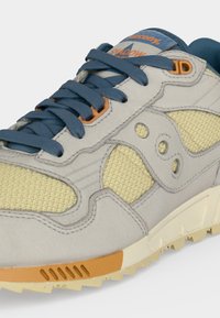 Γκρι και κίτρινο αθλητικό παπούτσι με μπλε κορδόνια, πορτοκαλί λεπτομέρειες, υφασμάτινα πάνελ με υφή και παχύ μπεζ πέλμα.